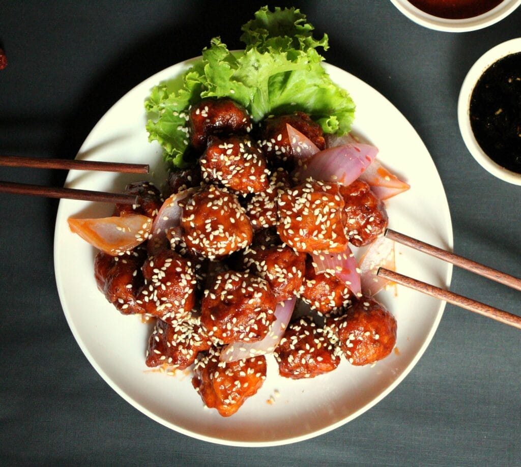 A gallery-worthy plate of sesame chicken garnished with green lettuce and onions, served with chopsticks. - The 108 Hotel Islamabad - Sesame & Soy Restaurant
